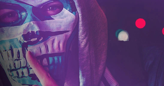 Close-up of man in a skull mask and hoody in dark purple light