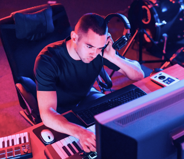 Man, with headphones in front of keyboard and PC