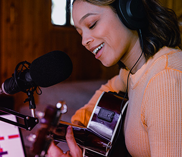 Record Vocals A close-up of a young woman playing guitar and singing into a microphone