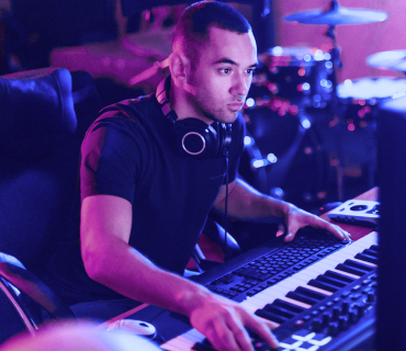 Man with headphones sitting at a table in front of keyboard and computer screen